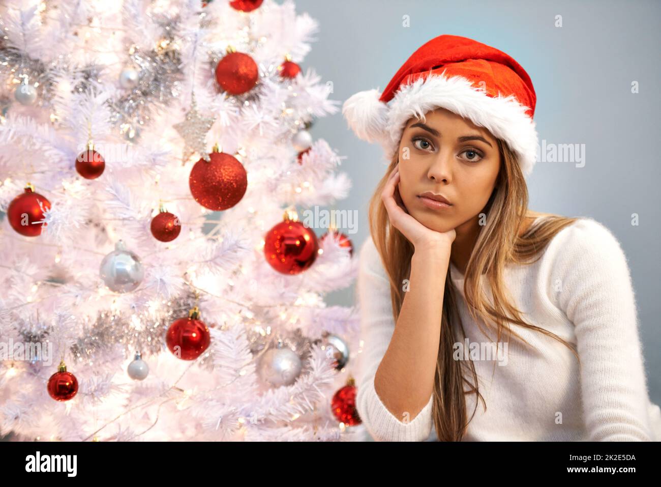Ich fühle mich dieses Weihnachten einsam. Porträt einer schönen jungen Frau, die traurig aussieht, während sie allein an einem Weihnachtsbaum sitzt. Stockfoto