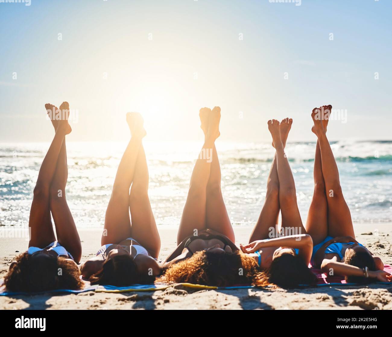 Lange, faule, strandige Tage. Aufnahme einer Gruppe junger Frauen, die sich mit ihren Beinen am Strand entspannen. Stockfoto