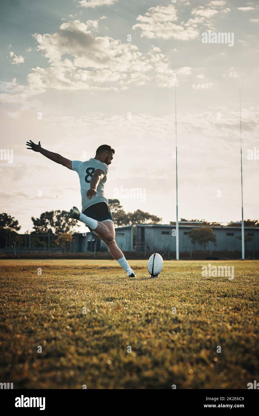 Seine Technik ist unübertroffen. Ganzkörperschuss eines hübschen jungen Rugby-Spielers, der tagsüber einen Ball auf dem Spielfeld tritt. Stockfoto