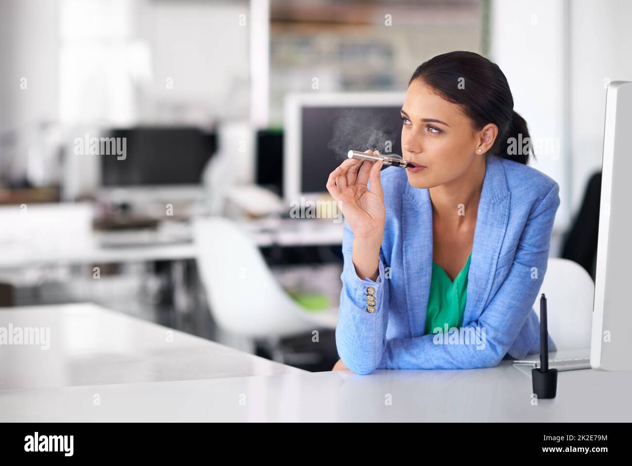 Zwischen den Besprechungen schnell ein Waper machen. Aufnahme einer Geschäftsfrau, die in einem Büro raucht und eine elektronische Zigarette verwendet. Stockfoto