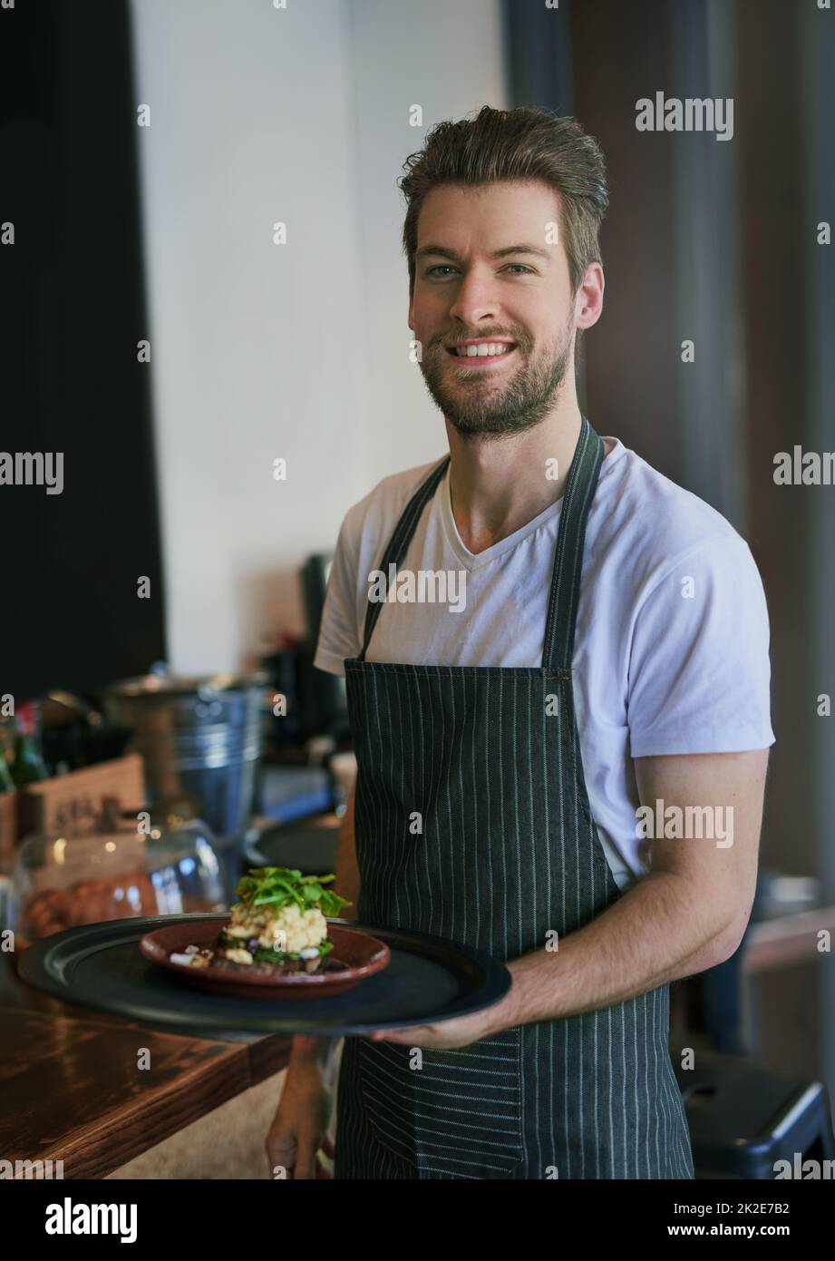 Service mit einem Lächeln. Zugeschnittenes Porträt eines jungen Kellners, der einen Auftrag an einen Kunden übergibt. Stockfoto