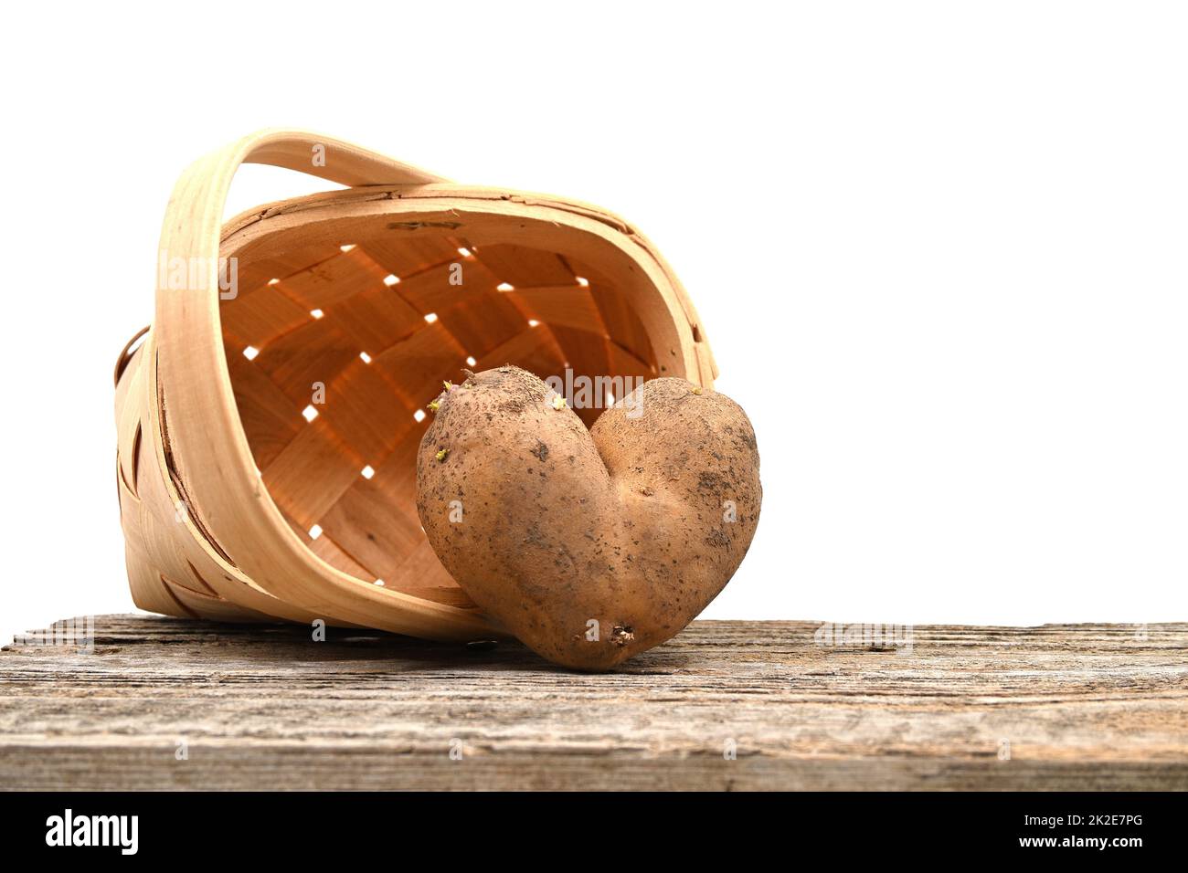 Herzförmige Kartoffel gegen einen gewebten Korb auf dem Tisch Stockfoto