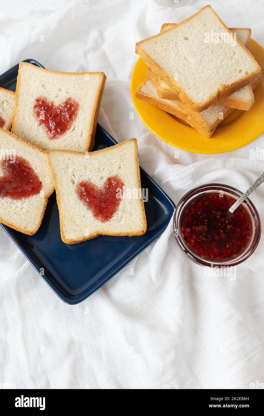Toast, auf dem das Herz aus Marmelade besteht. Überraschendes Frühstückskonzept im Bett. Romantik für St. Valentinstag. Stockfoto