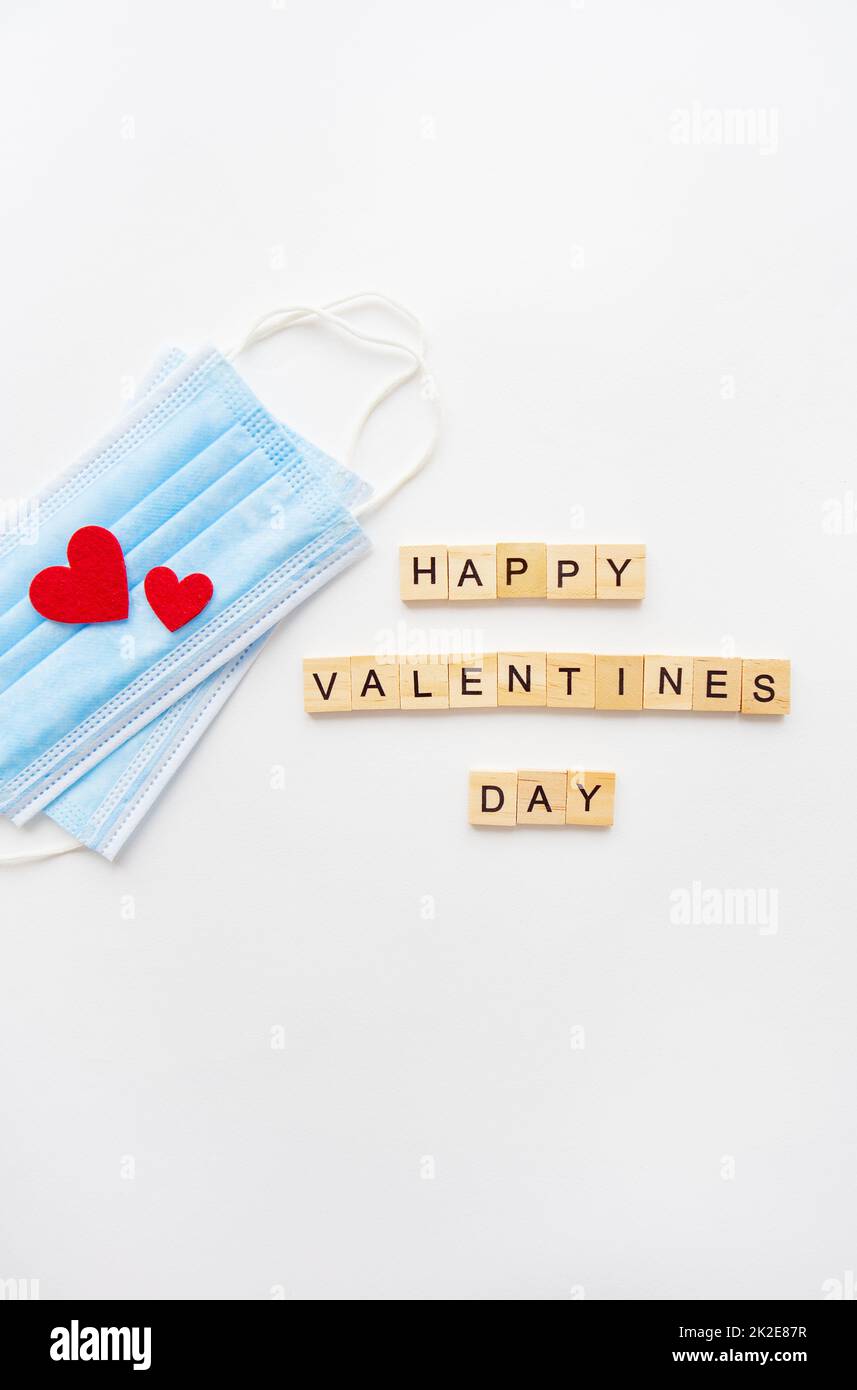 Konzept der Valentinstagsfeier. Hölzerne Inschrift Alles Liebe zum Valentinstag. Am 14.. Februar. Das Herz liegt auf medizinischen Masken, dem Kampf gegen das Coronavirus. Stockfoto