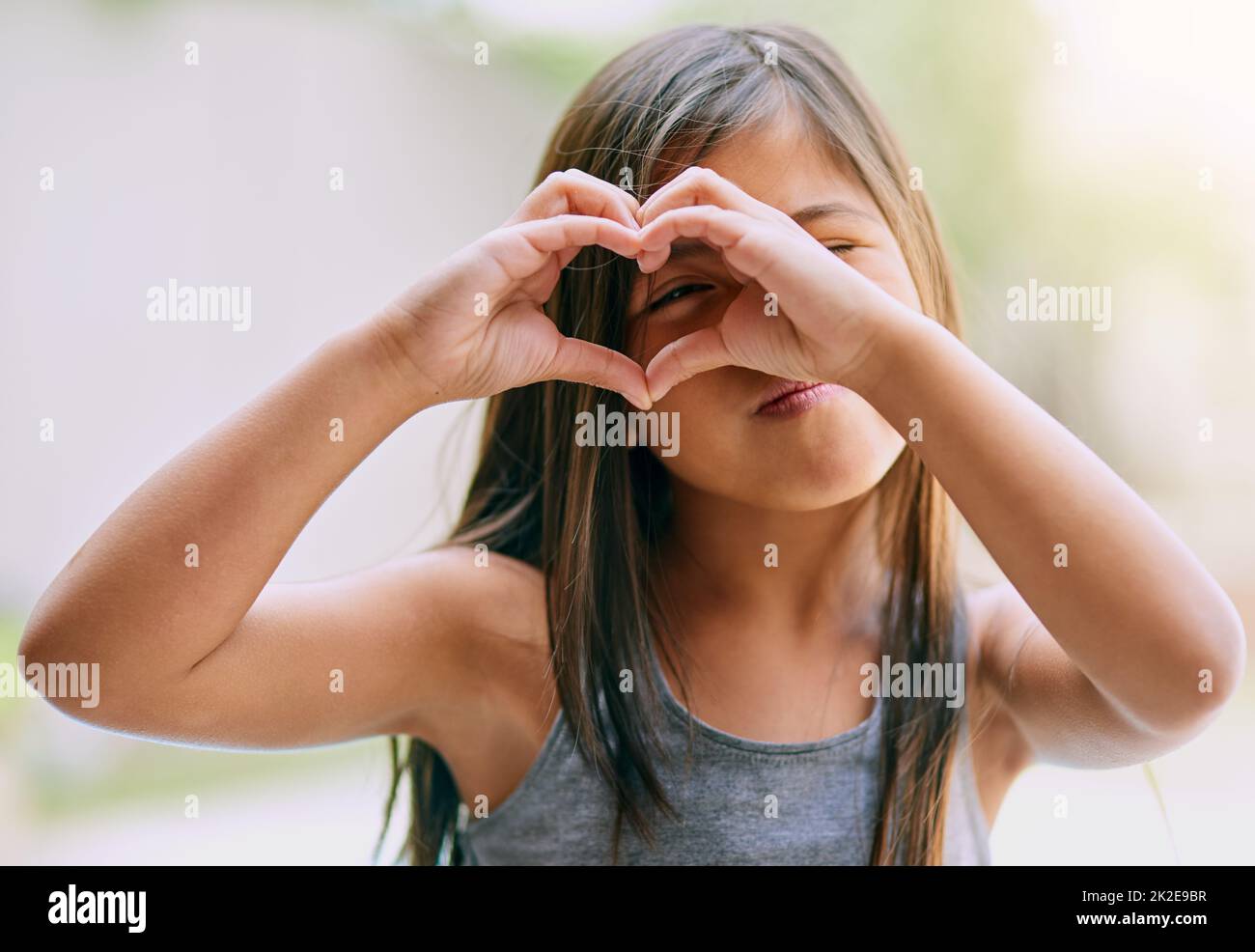 Das Leben mit Liebe und Glück füllen. Porträt eines kleinen Mädchens, das mit ihren Händen eine Herzgeste macht. Stockfoto