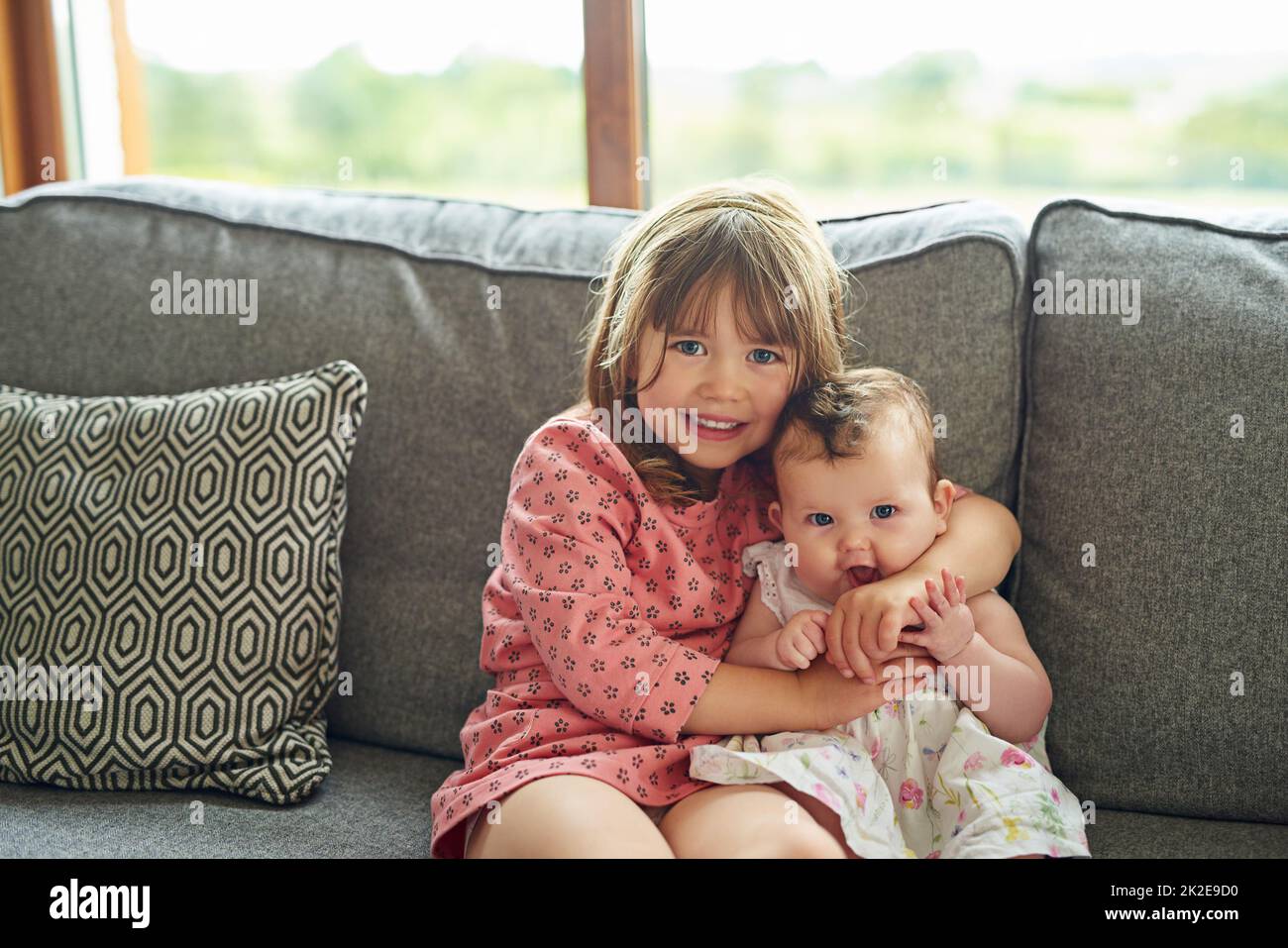 So glücklich, eine große Schwester zu sein. Porträt eines kleinen Mädchens, das sich zu Hause mit ihrer kleinen Schwester verklebt. Stockfoto