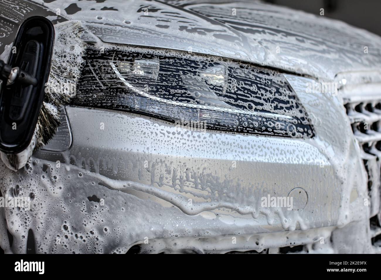 Anzeigeleuchte vorne Silber Auto in Waschstraße gewaschen, Pinsel, Anschläge in Shampoo und Schaum. Stockfoto