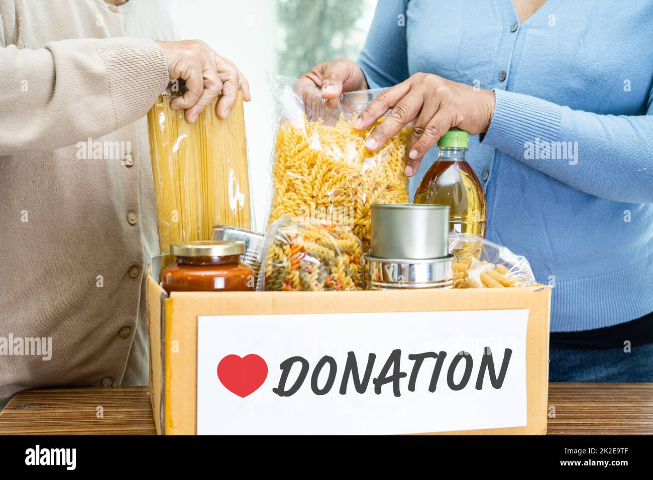 Freiwillige, die verschiedene trockene Lebensmittel in eine Spendenbox stecken, um Menschen zu helfen. Stockfoto