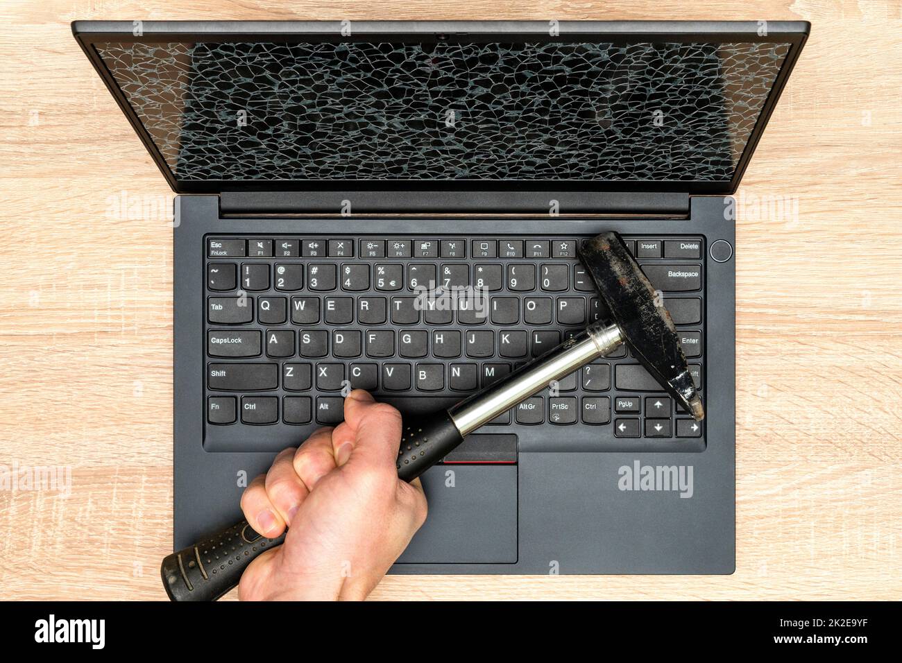 Hand mit einem Hammer und Laptop mit einem kaputten Bildschirm Stockfoto