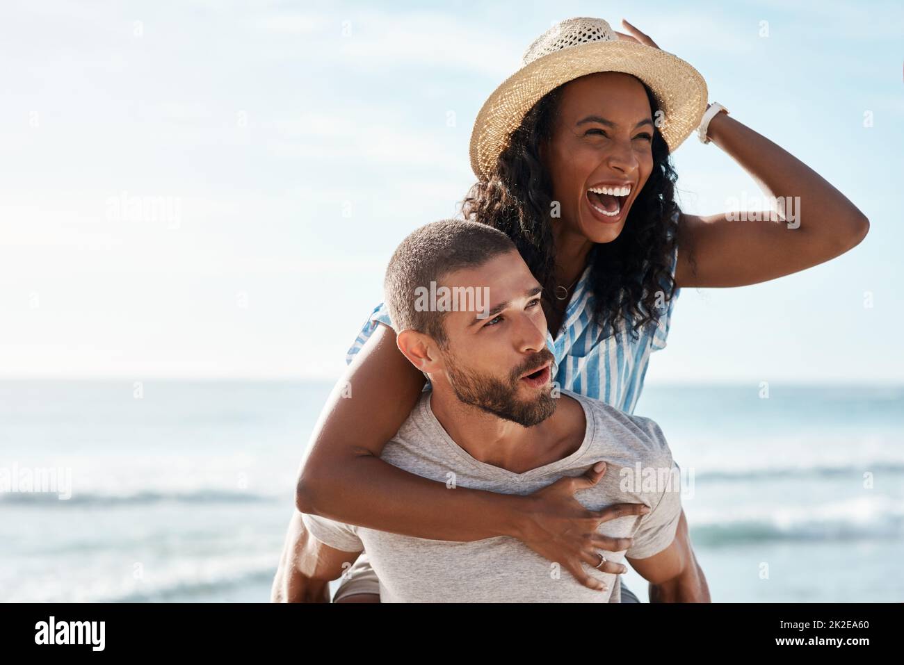 Sehen Sie sich die Sehenswürdigkeiten rund um das Meer an. Aufnahme eines jungen Mannes mit Huckepack seiner Freundin am Strand. Stockfoto