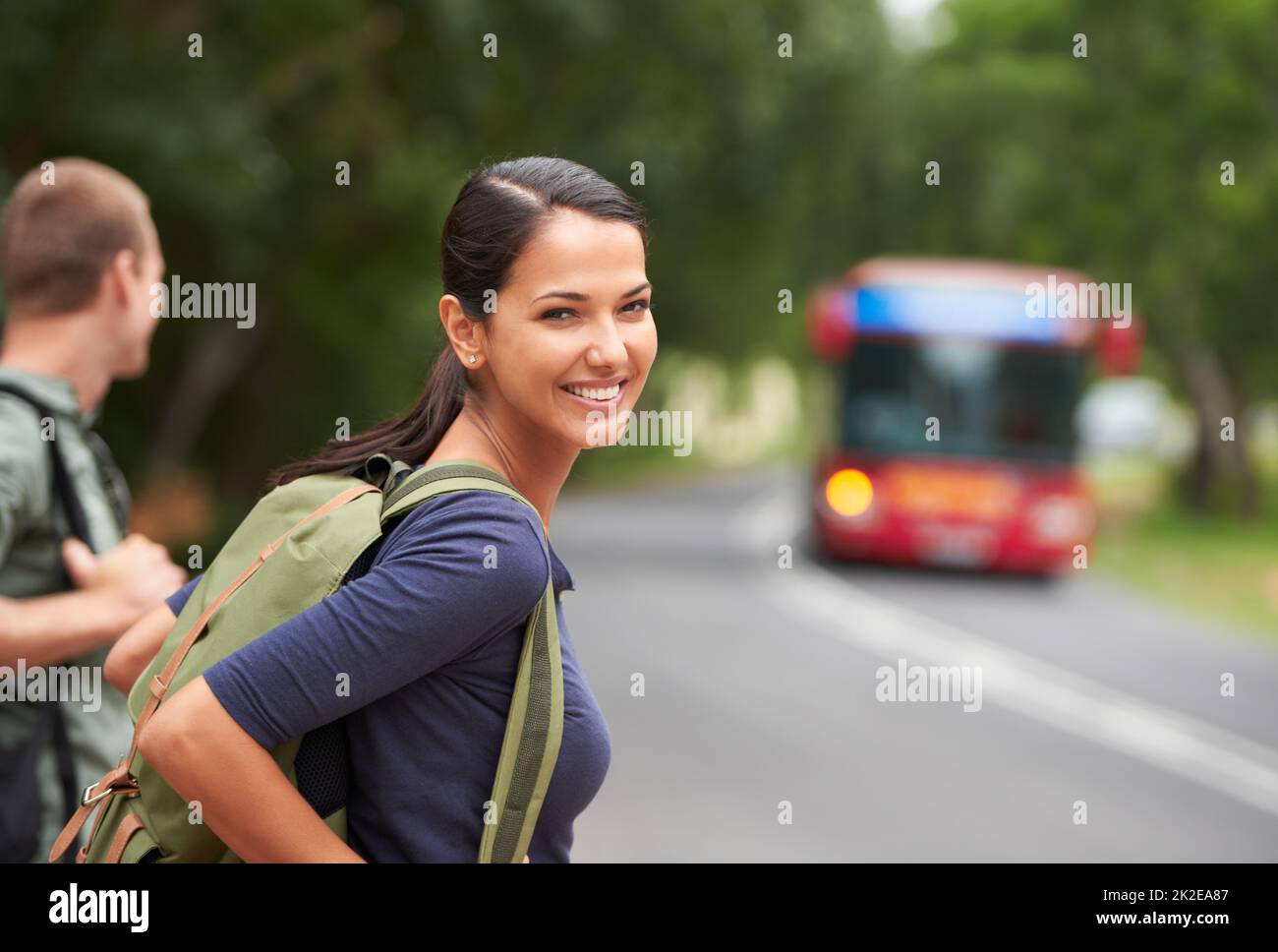 Sie gewöhnen sich immer noch an die Straßen. Eine schöne junge Frau, die einen Rucksack trägt, während sie auf einen Bus mit ihrem Mann wartet. Stockfoto