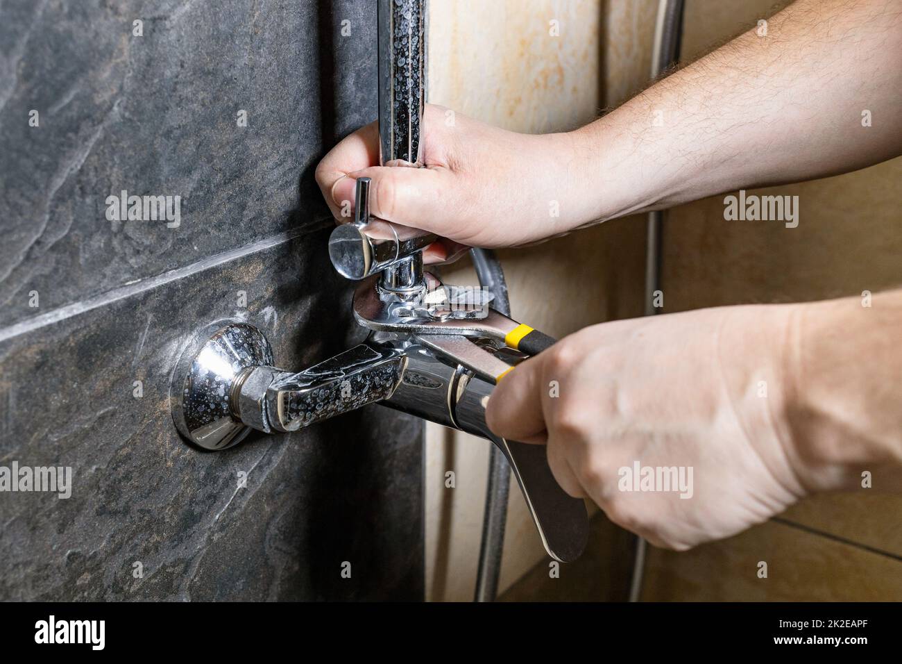 Der Klempner repariert alten Duschhahn an der gefliesten Wand Stockfoto
