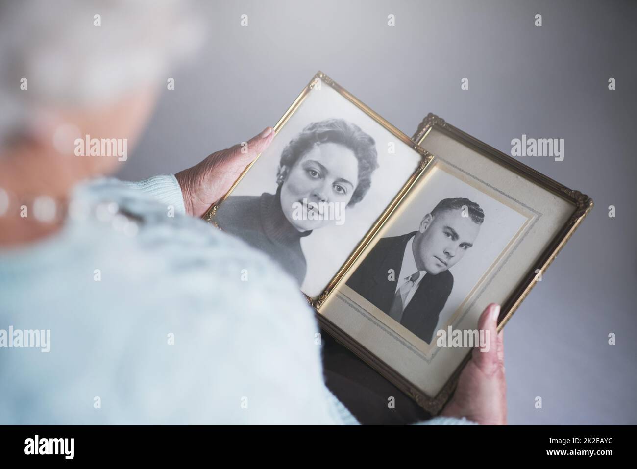 Blick durch Schnappschüsse aus der Vergangenheit. Ausgeschnittene Aufnahme einer älteren Frau, die alte Schwarz-Weiß-Fotos von einem Mann und einer Frau ansieht. Stockfoto