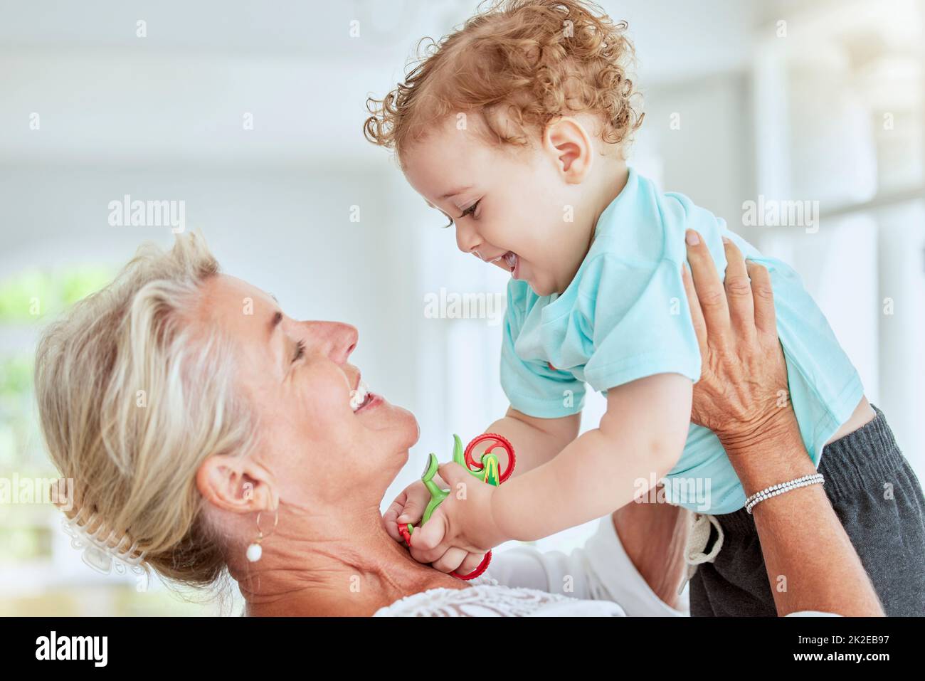 Familie, Liebe und Oma spielen mit Baby zu Hause, Spaß haben und genießen Sie die Zeit miteinander. Großmutter hebt sich glücklich, lächelt und lacht Stockfoto