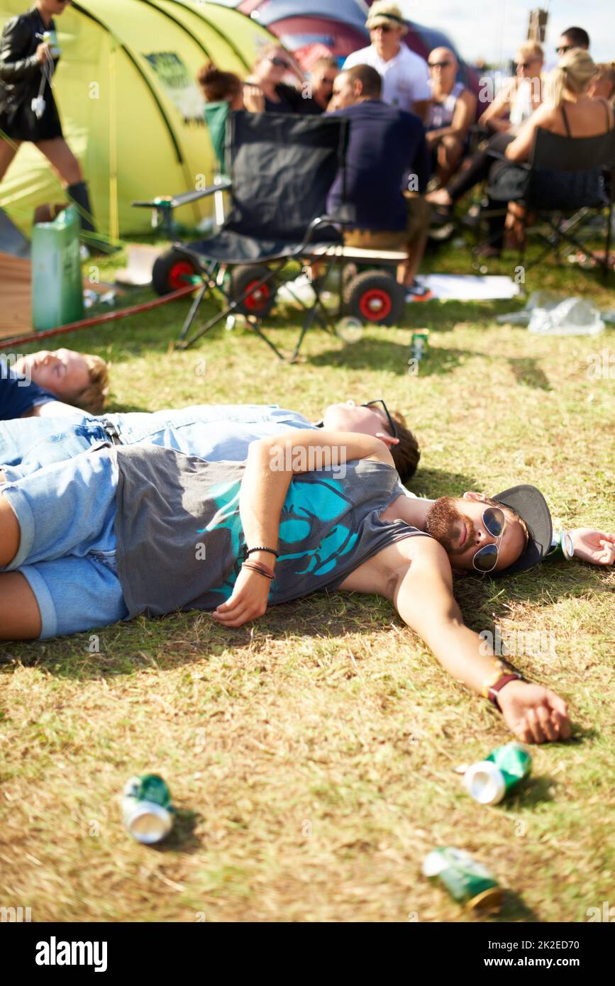 Wenn gute Zeiten schlecht werden. Aufnahme einer Gruppe von Männern, die auf dem Gras, umgeben von leeren Bierdosen, bei einem Festival im Freien ohnmächtig wurden. Stockfoto