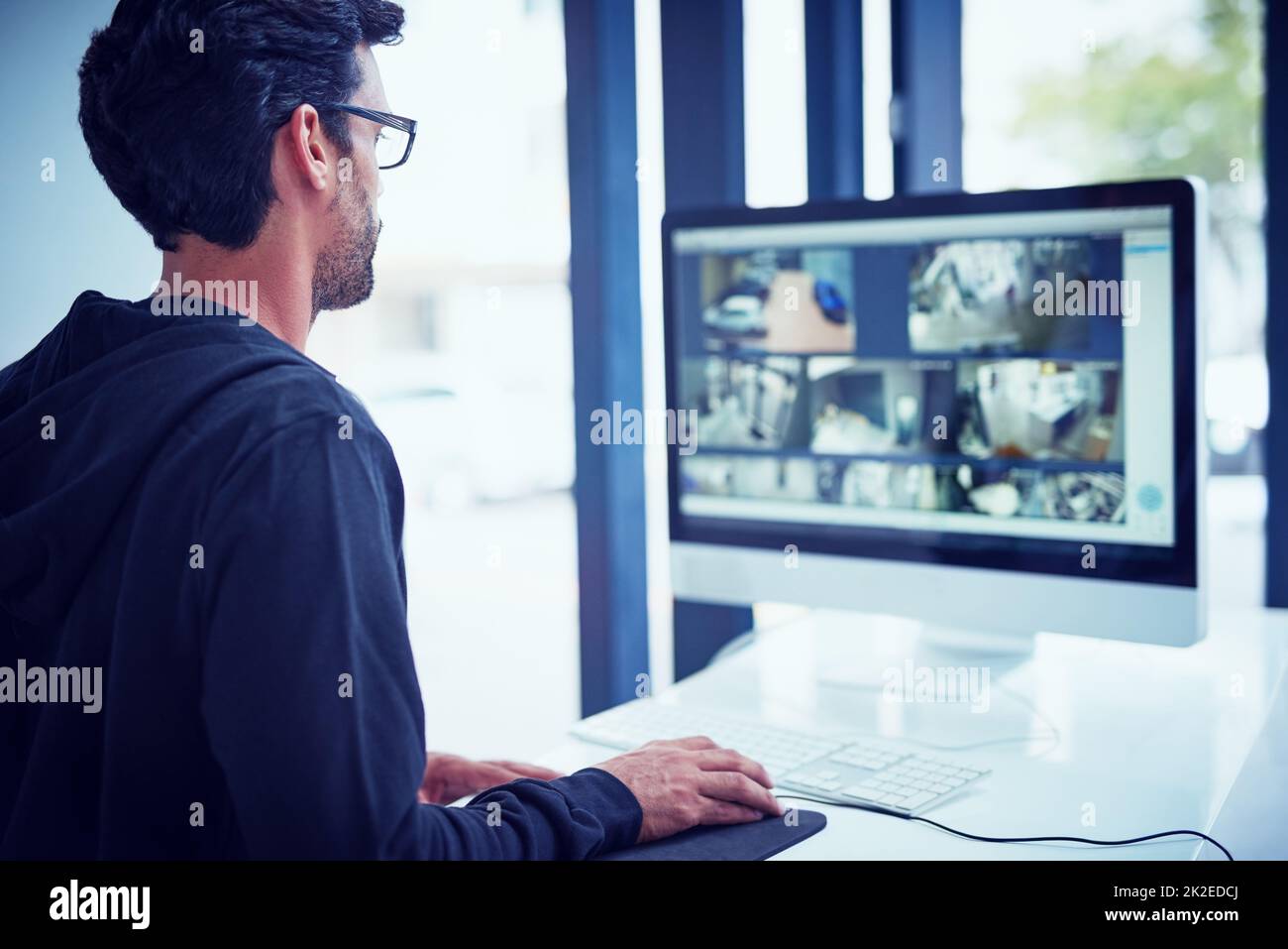 Nichts entgeht seiner Überwachung. Ausgeschnittene Aufnahme eines jungen Mannes, der Sicherheitsaufnahmen auf seinem Computer ansieht. Stockfoto