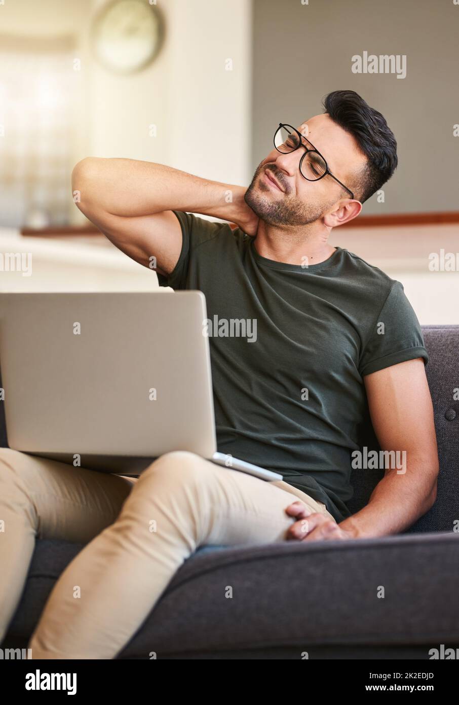 Ich denke, ich sitze vielleicht zu lange. Aufnahme eines hübschen jungen Mannes, der bei der Arbeit am Laptop zu Hause unter Nackenschmerzen leidet. Stockfoto
