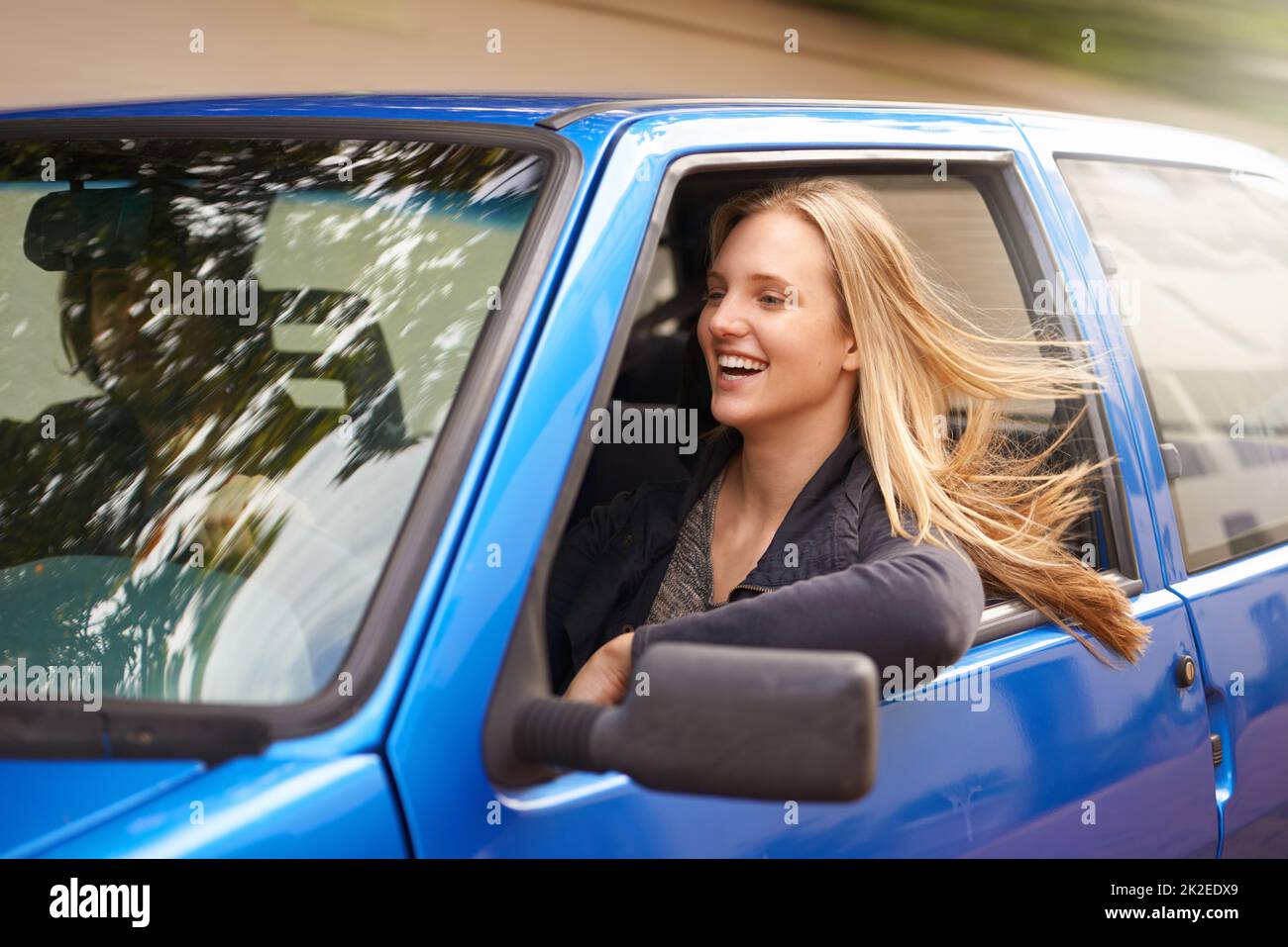 Unterwegs. Eine junge Frau, die den Wind in ihren Haaren durch ein offenes Autofenster spürt. Stockfoto