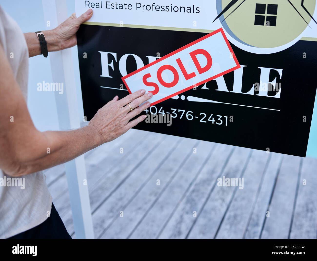 Eine andere Immobilie verkauft. High-Angle-Aufnahme einer unkenntlich weiblichen Immobilienmaklerin, die ein verkauftes Schild über ein Verkaufsboard klebt. Stockfoto