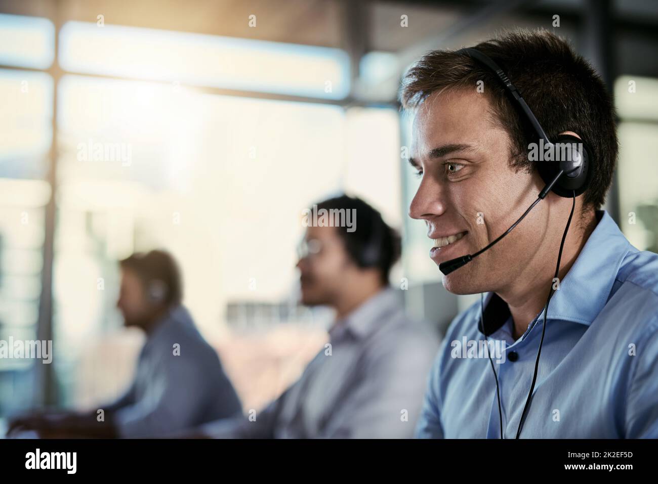 Zuverlässiger Kundendienst ist nur einen Anruf entfernt. Ein Bild eines Callcenter-Agenten, der in einem Büro arbeitet, mit seinen Kollegen im Hintergrund. Stockfoto