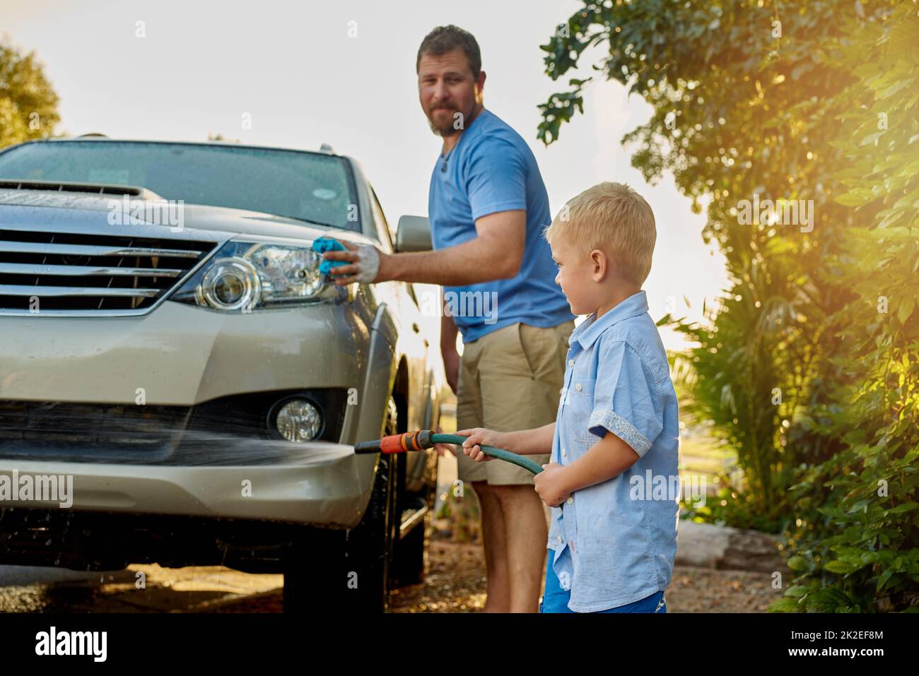 Er mag jung sein, aber er ist immer noch sehr hilfsbereit. Ausgeschnittene Aufnahme eines Vaters und eines Sohnes, der zusammen ein Auto wascht. Stockfoto