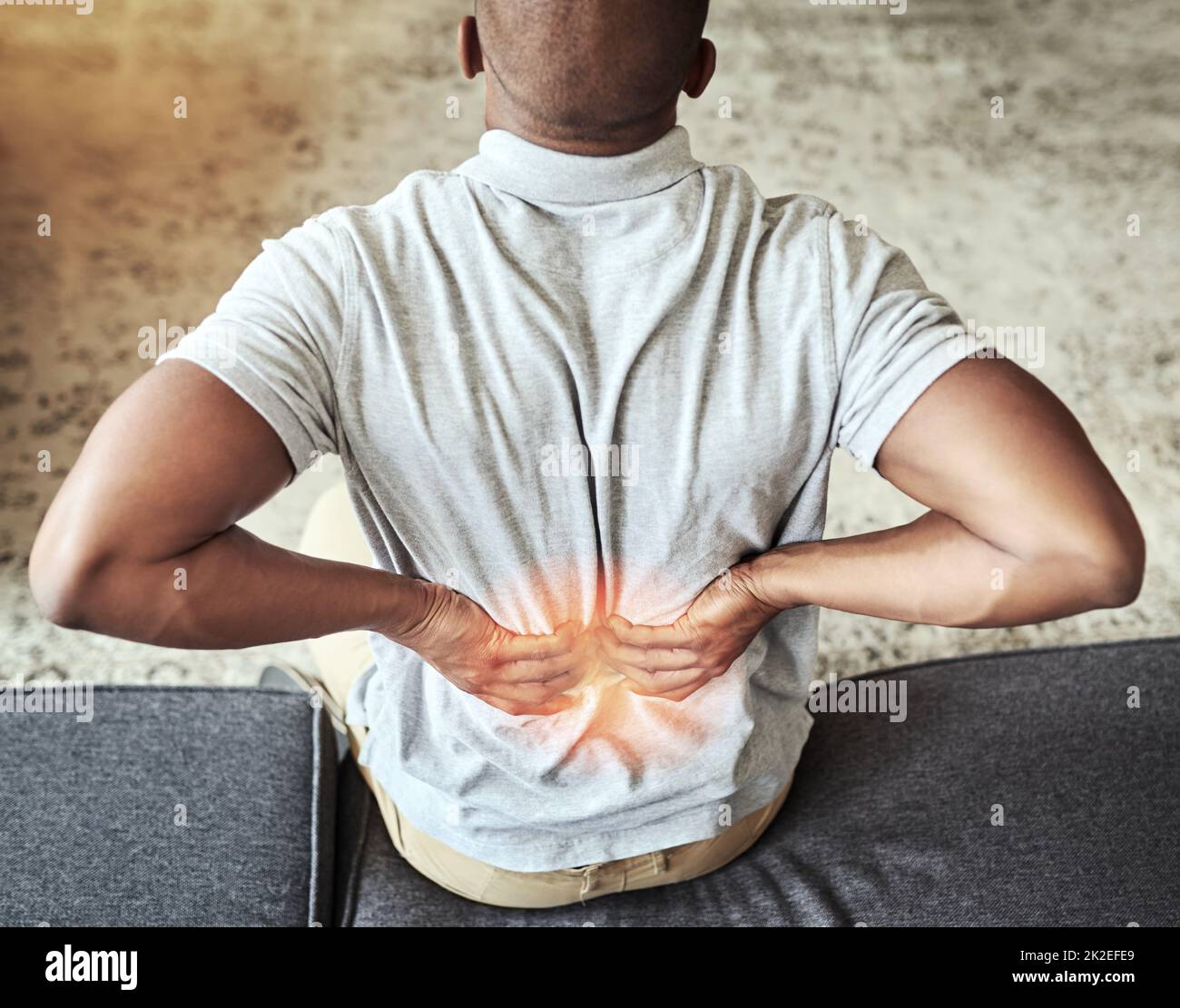 Ich muss regelmäßig einige Strecken machen. Rückansicht eines nicht erkennbaren Mannes, der sich unwohl den Rücken hielt, während er zu Hause auf einer Couch saß. Stockfoto