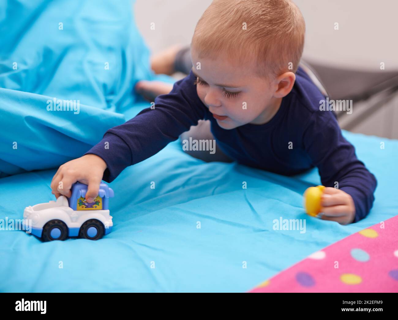 Vrooommm. Ein kleiner Junge, der mit einem Spielzeugauto auf seinem Bett spielt. Stockfoto