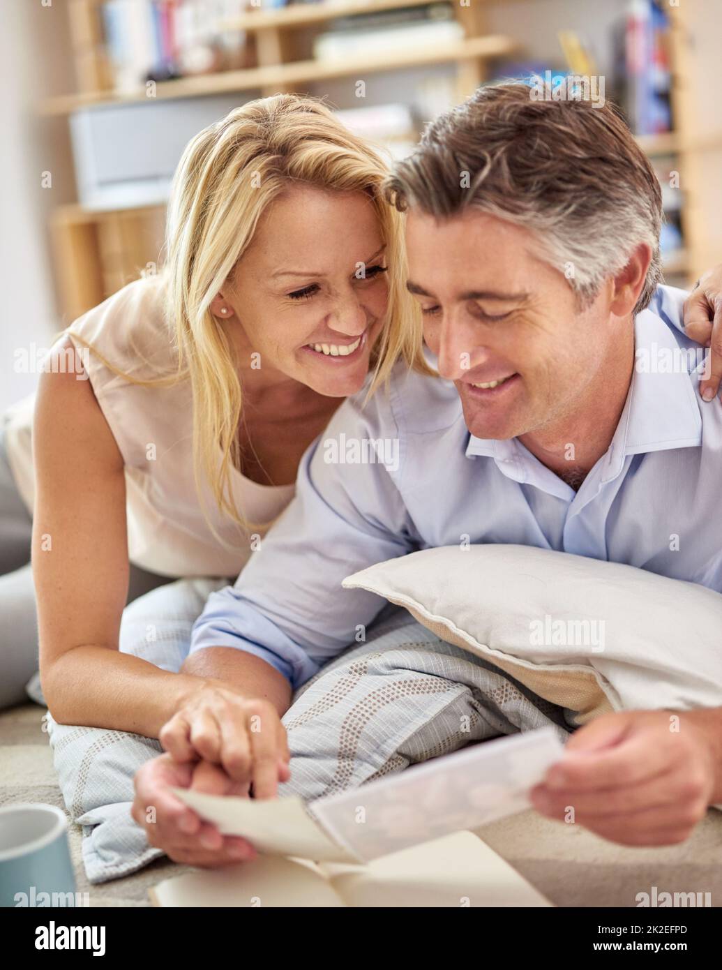 Eine Reise in die Gedächtnisspur. Aufnahme eines lächelnden, reifen Paares, das auf dem Boden des Wohnzimmers liegt und Fotos ansieht. Stockfoto