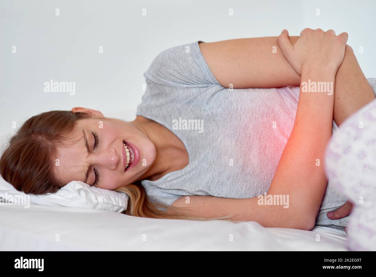 Dieser Schmerz ist viel zu unerträglich. Ein kurzer Schuss einer jungen Frau mit Magenschmerzen, rot hervorgehoben. Stockfoto