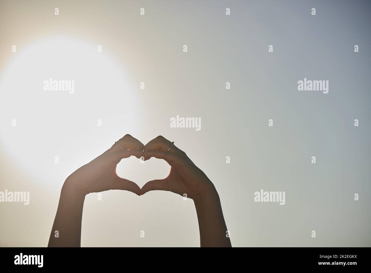 Liebe ohne Grenzen. Eine kurze Aufnahme einer Frau, die mit ihren Händen gegen einen blauen Himmel eine Herzform formt. Stockfoto