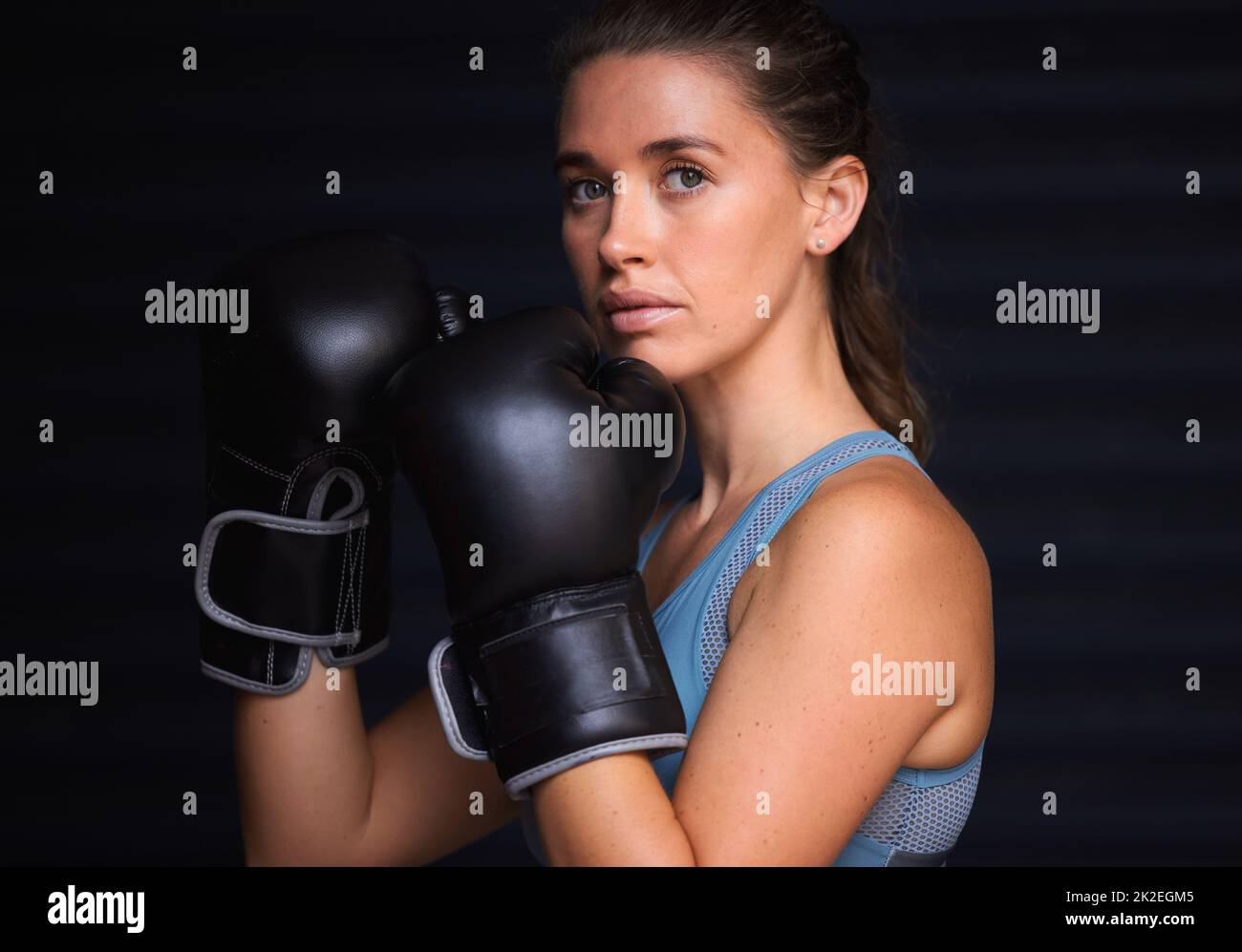 Unzerbrechlich und unbesiegt. Porträt einer jungen Frau mit Boxhandschuhen vor schwarzem Hintergrund. Stockfoto