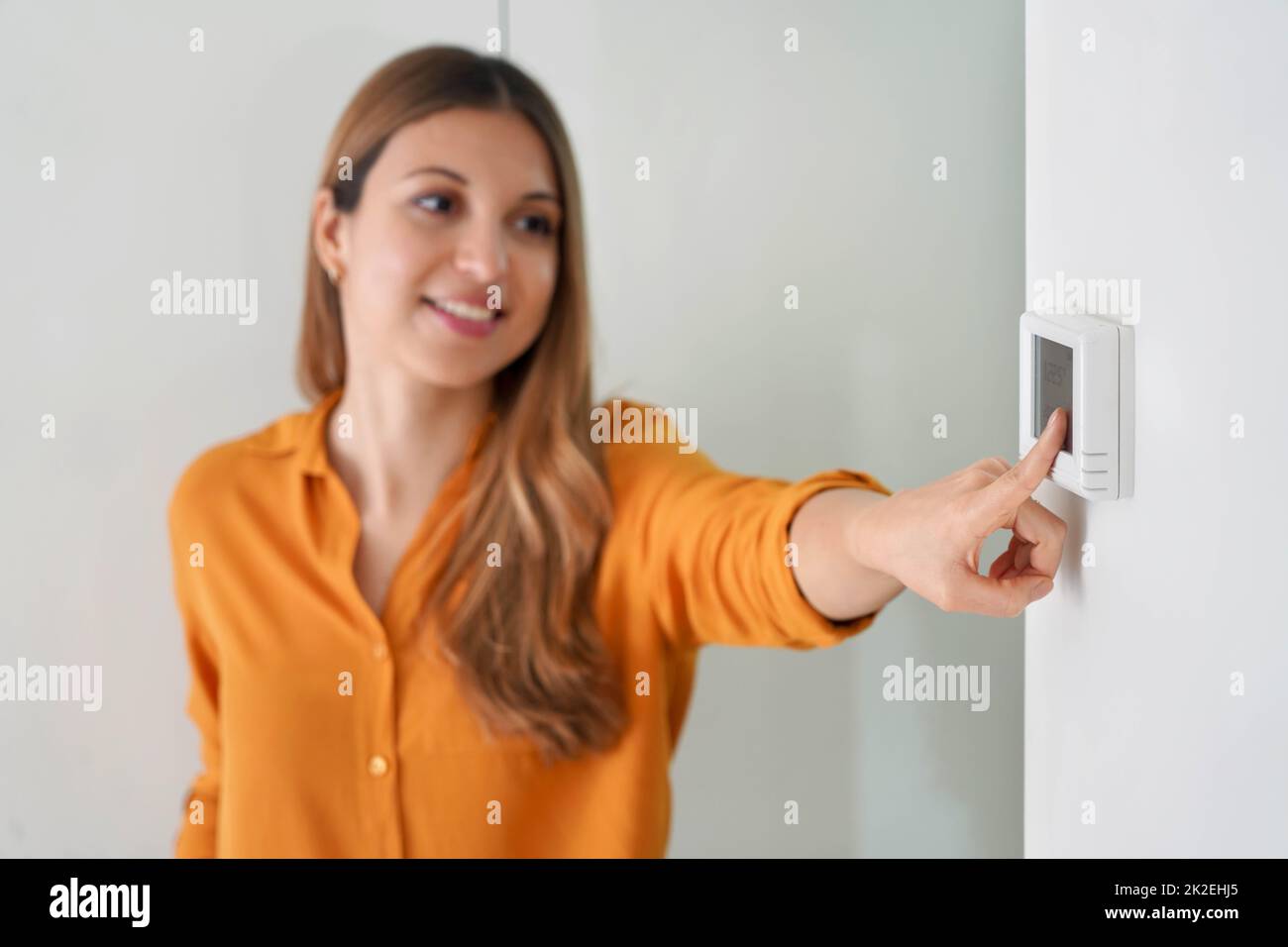 Senken der Temperatur zur Energieeinsparung. Junge Frau, die zu Hause den digitalen Thermostat für die Zentralheizung justiert. Konzentrieren Sie sich auf die Hand. Stockfoto