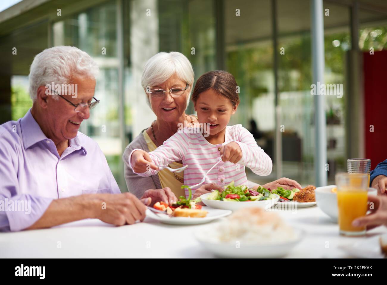 Für Oma und Opa aufhaufengend. Aufnahme einer Enkelin, die mit ihren Großeltern sitzt, während sie draußen ein Essen genießt. Stockfoto