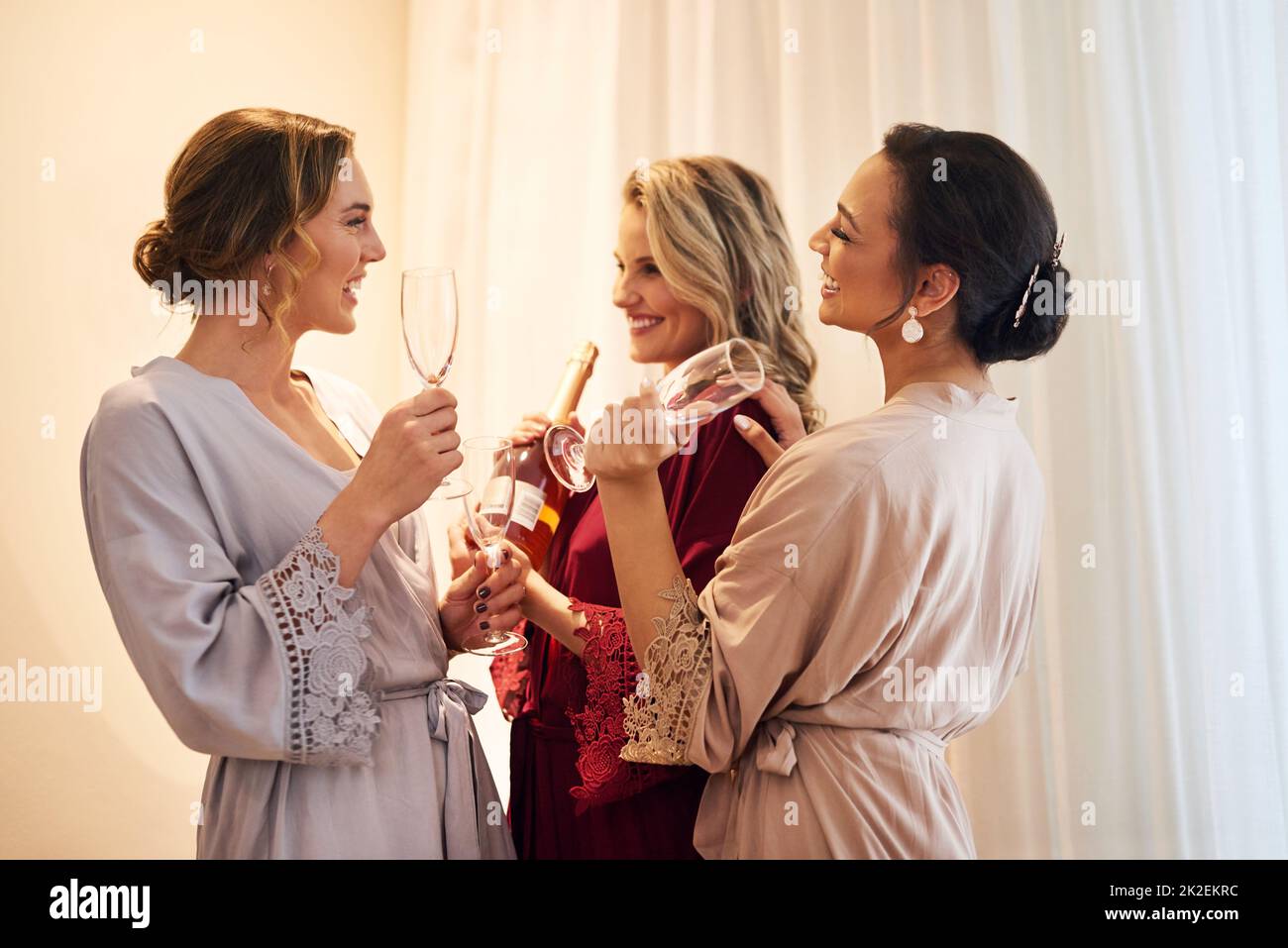 Ein wenig Champagner macht das. Eine kurze Aufnahme einer schönen jungen Braut und ihrer Brautjungfern, die vor der Hochzeit Champagner in ihrem Ankleidezimmer hatten. Stockfoto