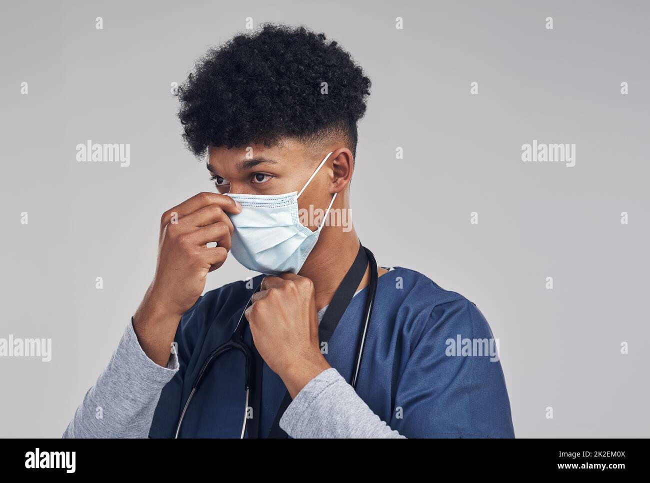 Deine Maske sollte deine Nase und deinen Mund bedecken. Aufnahme eines Krankenpflegers, der eine OP-Maske trägt, während er vor einem grauen Hintergrund steht. Stockfoto