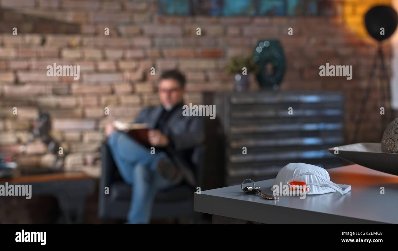 Mann liest zu Hause - Virenschutzmaske auf dem Schreibtisch Stockfoto