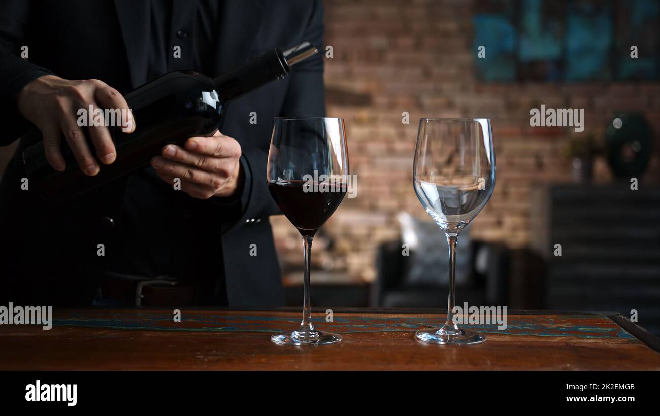 Ein Mann, der zu Hause Rotwein in Weingläser gießt Stockfoto