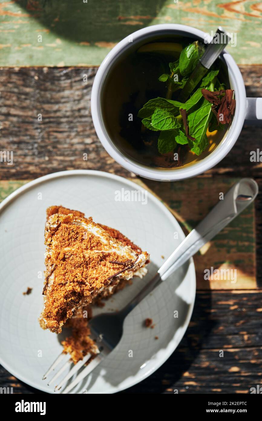 Ein großes Stück Kuchen auf Honigkuchen mit einem Becher schwarzen Tees mit Zitrone und Minze. Vertikales Foto. Stockfoto