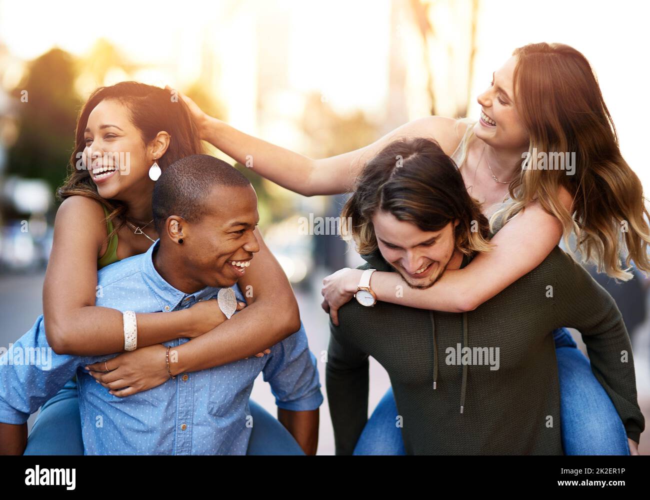 Doppel-Dating mit Paar, das weiß, wie man Viel Spaß. Aufnahme von zwei glücklichen jungen Paaren, die gemeinsam eine Huckepack-Fahrt durch die Stadt Unternehmen. Stockfoto