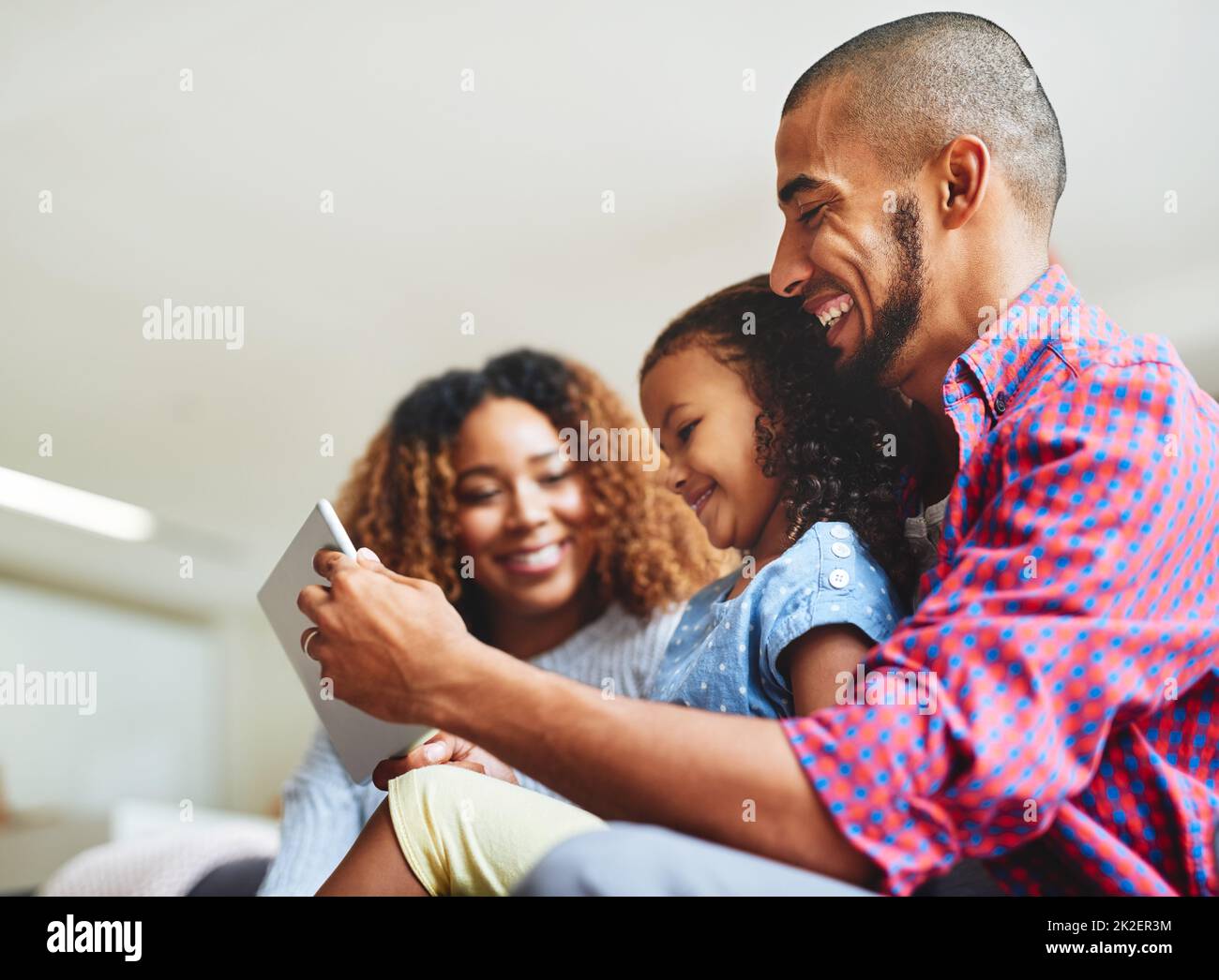 Familienzeit und Bildschirmzeit kombiniert. Aufnahme eines entzückenden kleinen Mädchens und ihrer Eltern, die zu Hause ein digitales Tablet auf dem Sofa benutzen. Stockfoto