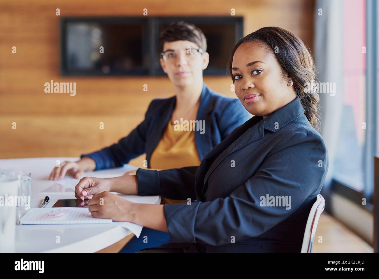 Im Sitzungssaal wird Geschäfte erledigt. Zugeschnittenes Porträt einer Geschäftsfrau, die im Sitzungssaal sitzt, mit einem Kollegen im Hintergrund. Stockfoto