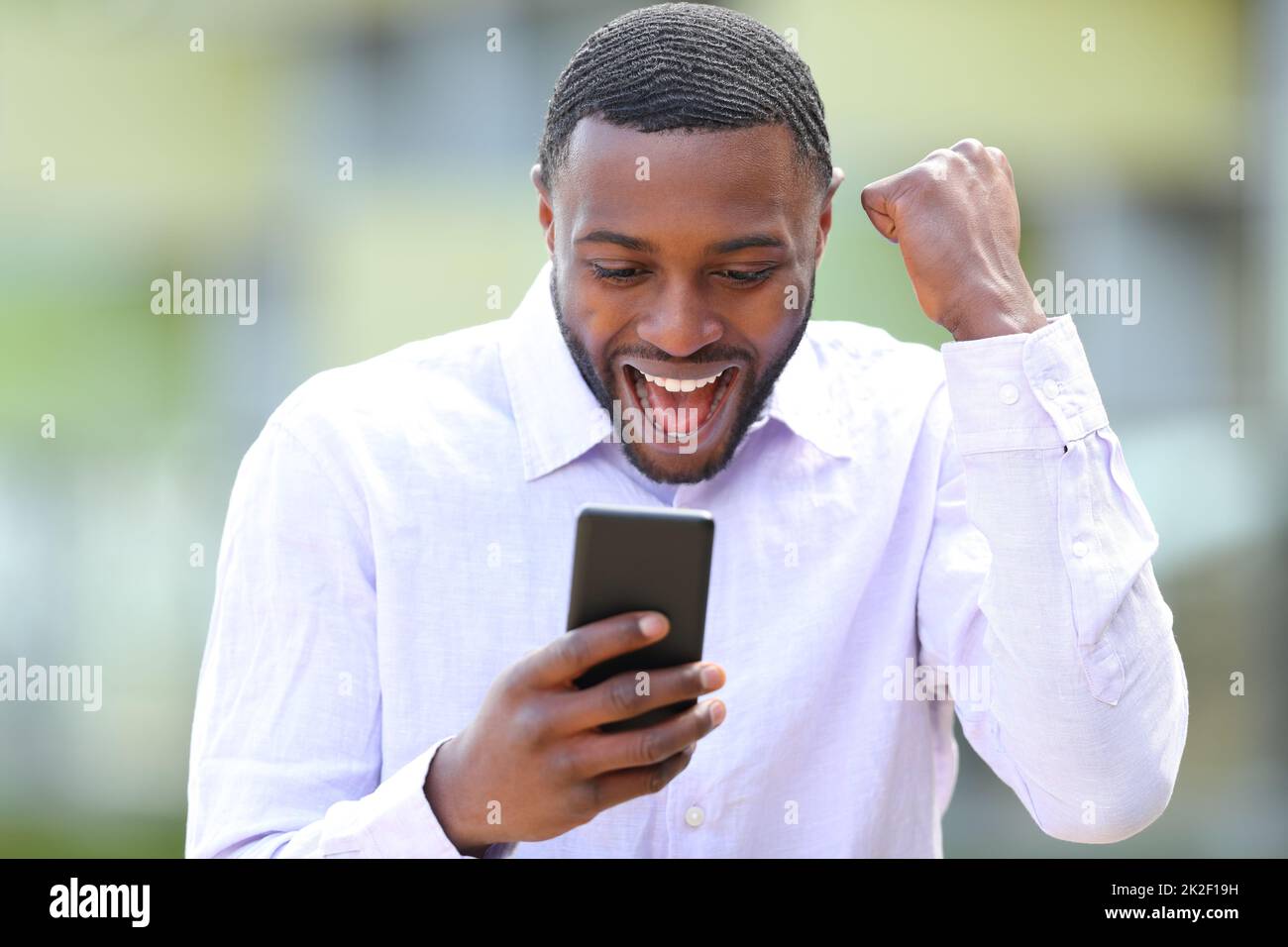 Aufgeregter Mann mit schwarzer Haut, der draußen sein Handy streichelt Stockfoto