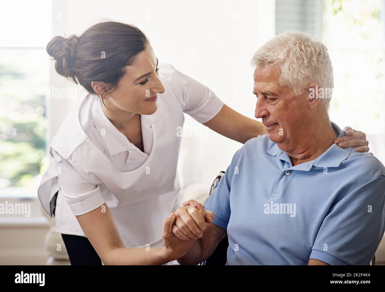 Häusliche Pflege mit Mitgefühl. Aufnahme eines Betreuers, der einem älteren Mann im Rollstuhl zu Hause hilft. Stockfoto