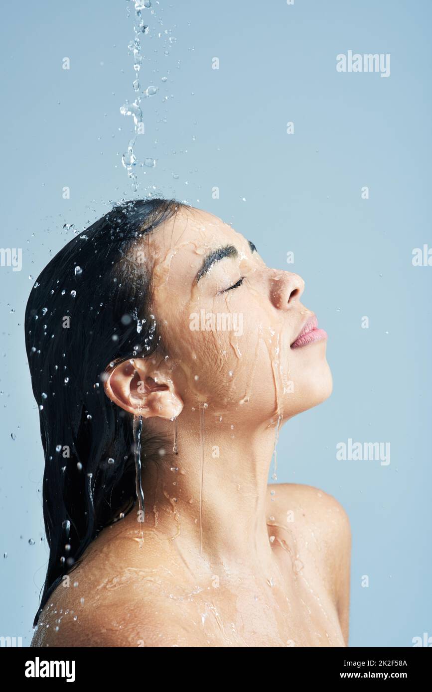 Lange Dusche nach einem langen Tag. Aufnahme einer jungen Frau, die vor blauem Hintergrund duscht. Stockfoto
