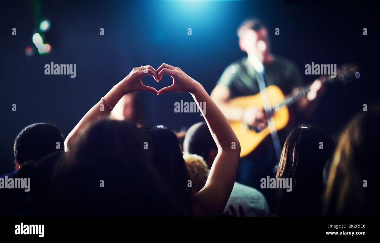 Aus Liebe zur Musik. Eine kurze Aufnahme von Händen einer Frau, die sich nicht wiedererkennen lassen und eine Herzform bilden, während ein Musiker bei einem Konzert in der Nacht auftritt. Stockfoto