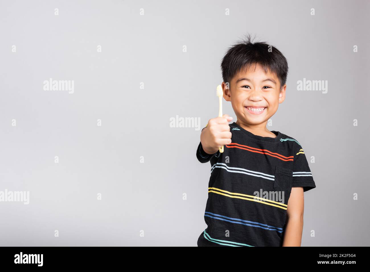 Der kleine süße Junge von 5-6 Jahren zeigt Zähne putzen und lächeln im Studio, isoliert Stockfoto