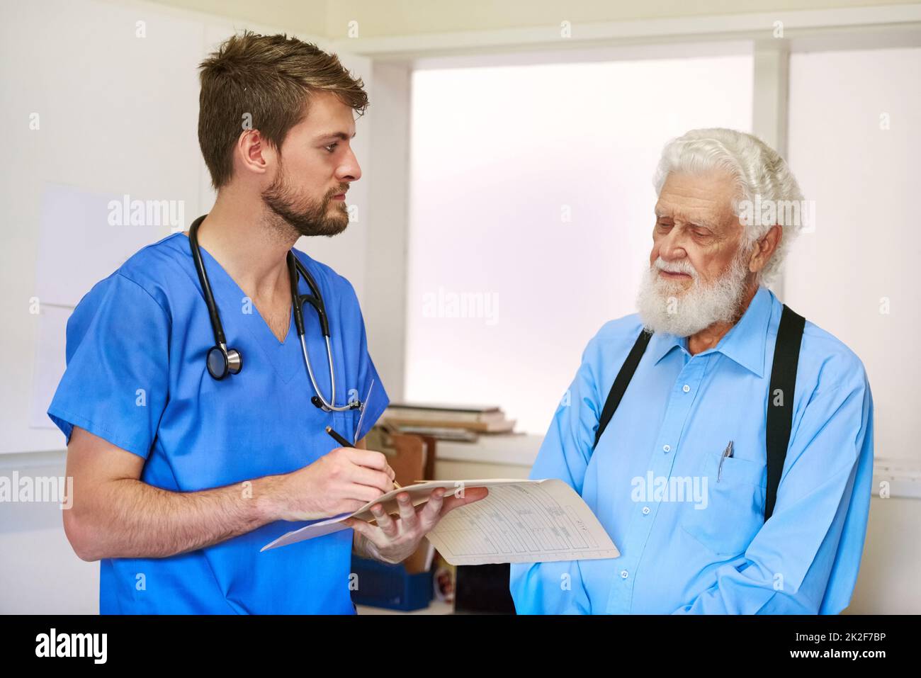 Welche anderen Symptome haben Sie erlebt? Aufnahme eines jungen Arztes und seines älteren Patienten, die gemeinsam über seine Krankenakten diskutierten. Stockfoto