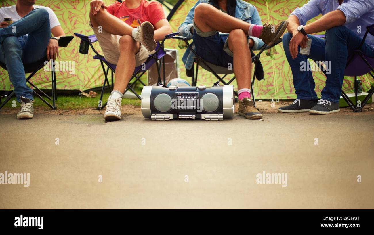Chillen im Takt. Vier Freunde genießen Musik von einer Stereoanlage, während sie auf Campingstühlen bei einem Musikfest sitzen. Stockfoto