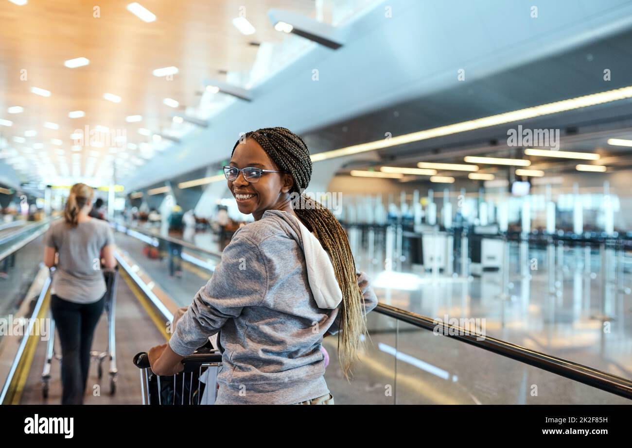 Gepäck Check-in, hier kommen wir. Rückfahrporträt einer attraktiven jungen Frau, die durch einen Flughafen läuft. Stockfoto