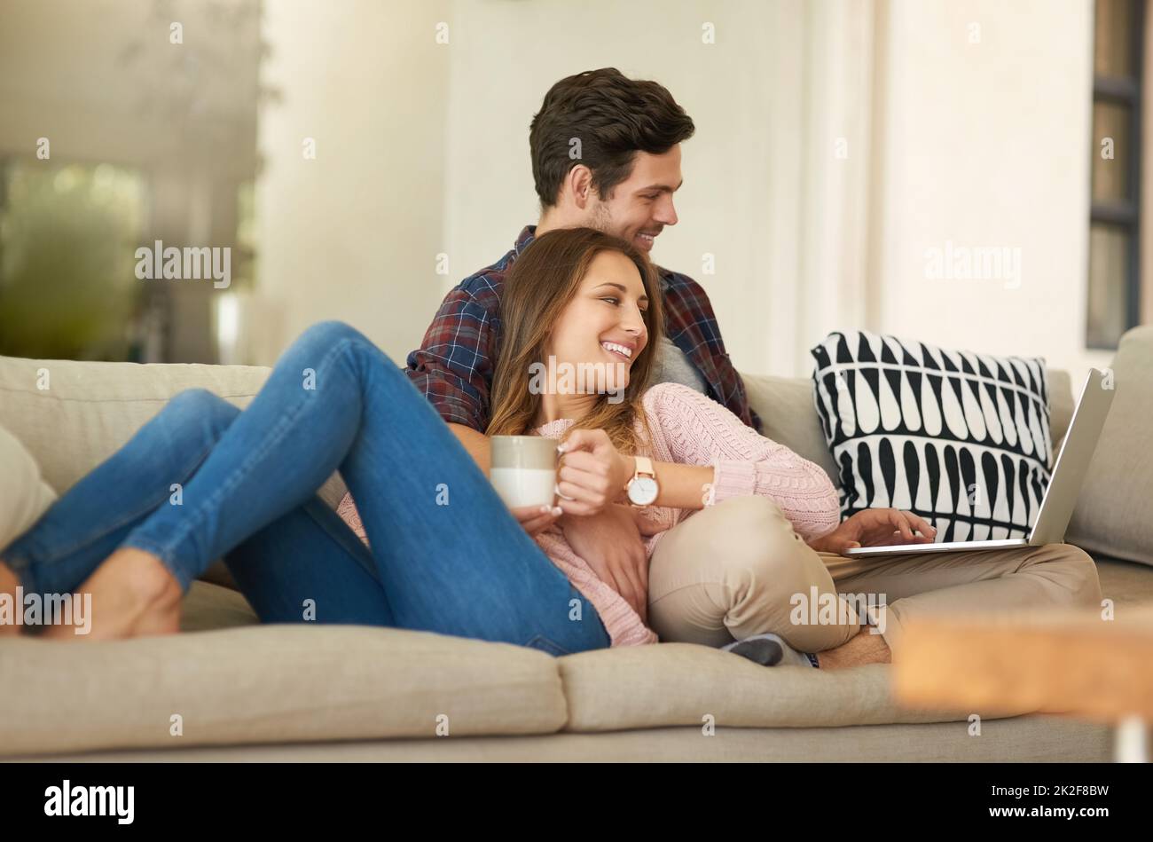 Gemütliche Wochenenden auf der Couch. Aufnahme eines glücklichen jungen Paares, das einen Laptop zusammen benutzt, während es sich zu Hause auf dem Sofa entspannt. Stockfoto